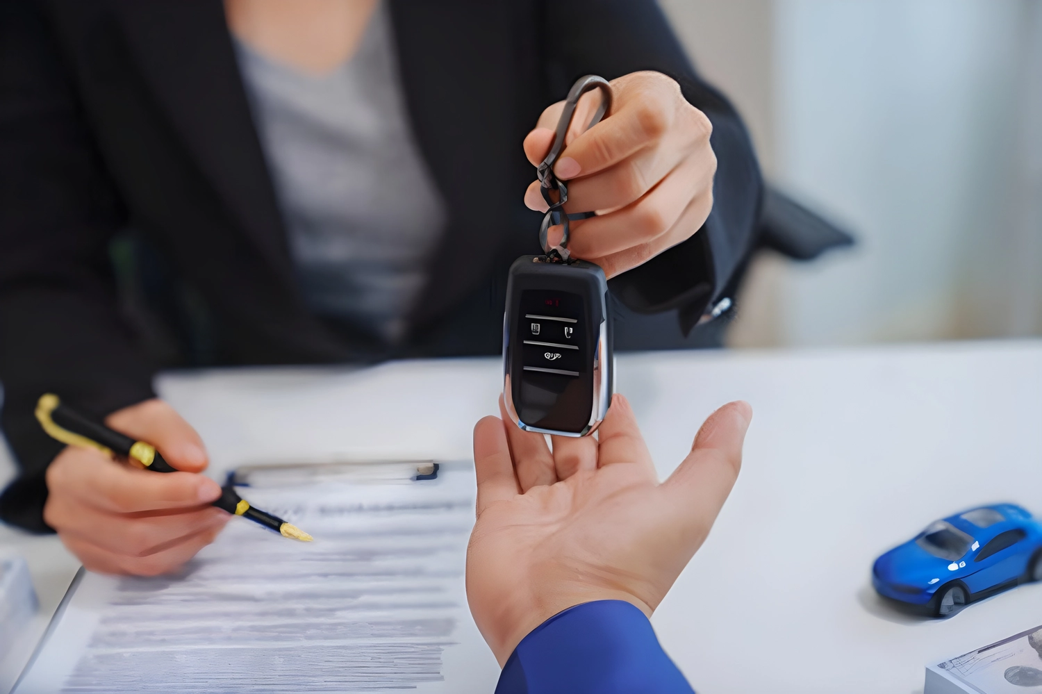 KFZ-Sachverständigenbüro - Peter Kühn - Ein asiatischer Verkäufer mittleren Alters in einem Anzug bedient eine Käuferin an einem Schreibtisch.